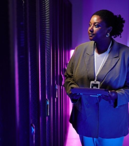 Portrait of female system administrator inspecting data network in server room lit by neon light, copy space